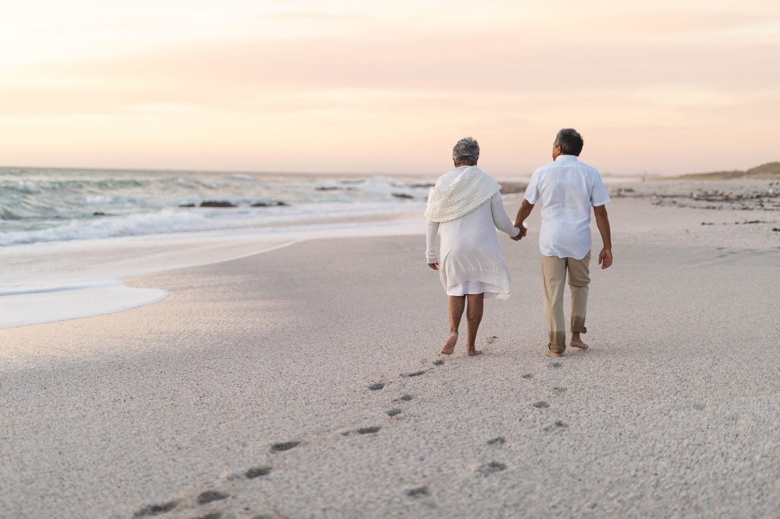 Life Settlements - A senior couple walking along the beach with their backs to us. ELIGIBILITY FOR VIATICAL SETTLEMENTS