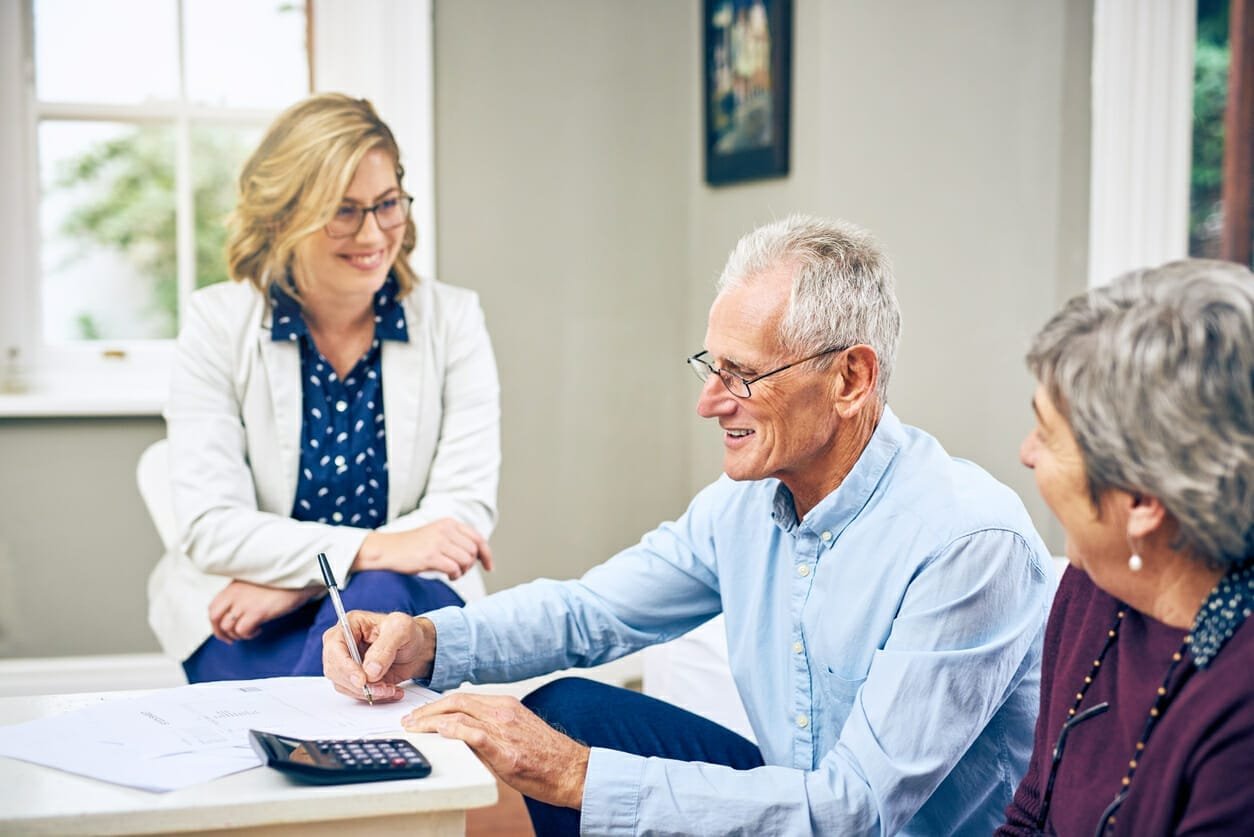 Life Settlement Qualifications - a Senior couple smiling while signing a contract. How life settlement brokers can help