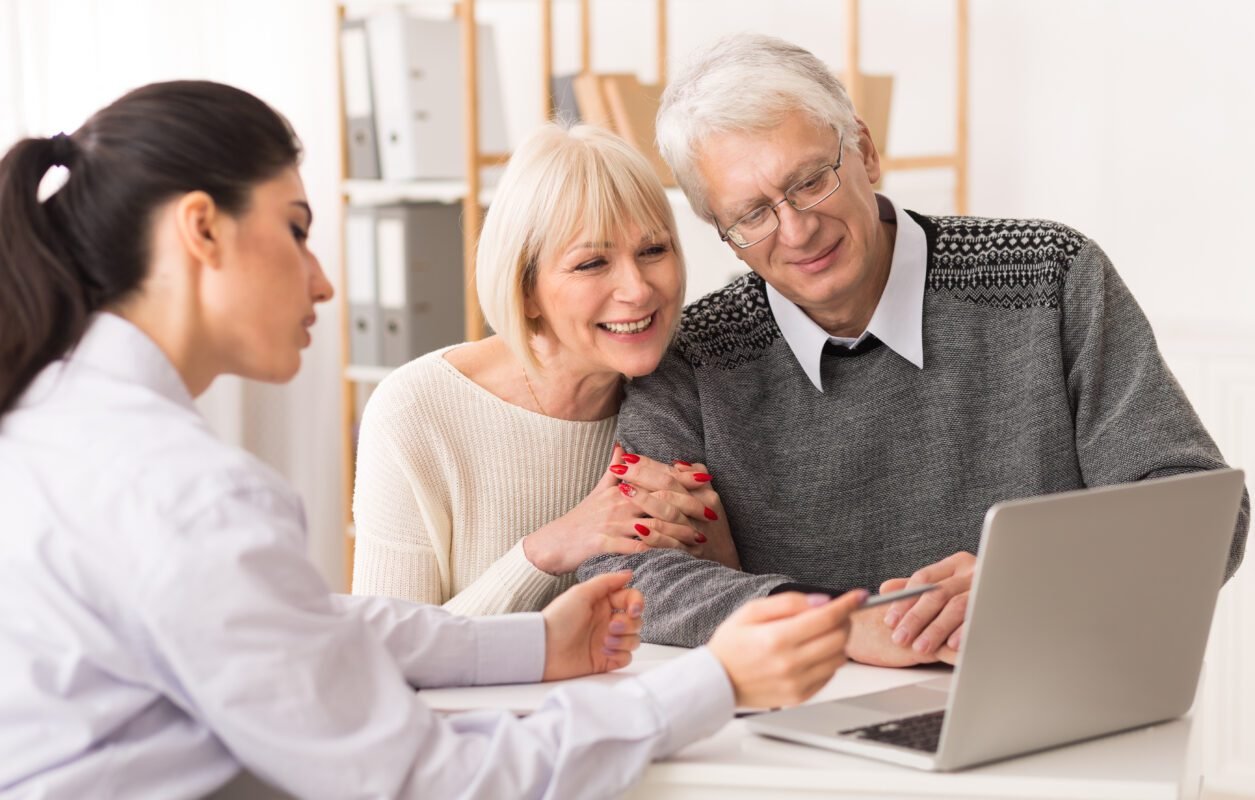 Senior couple meeting financial adviser for life insurance settlement, looking at laptop in office.