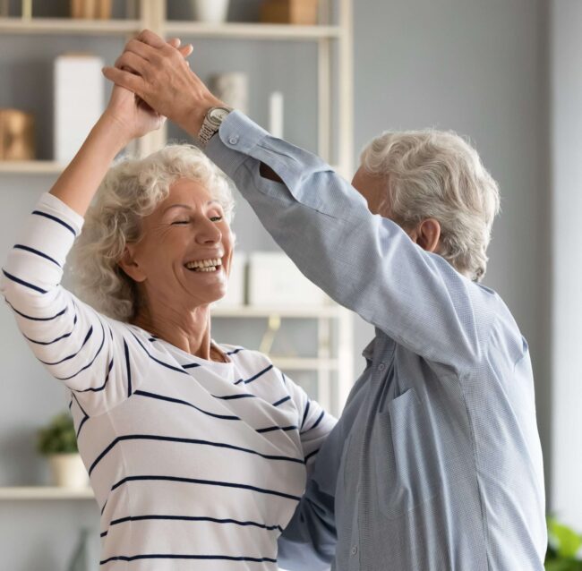 Life Settlement Broker – Overjoyed mature husband and wife dance in living room Life Settlement Broker - Overjoyed mature husband and wife dance in living room