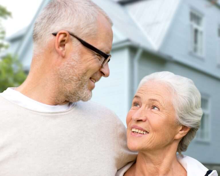Viatical Settlement vs Life Settlement - happy senior couple hugging over house background