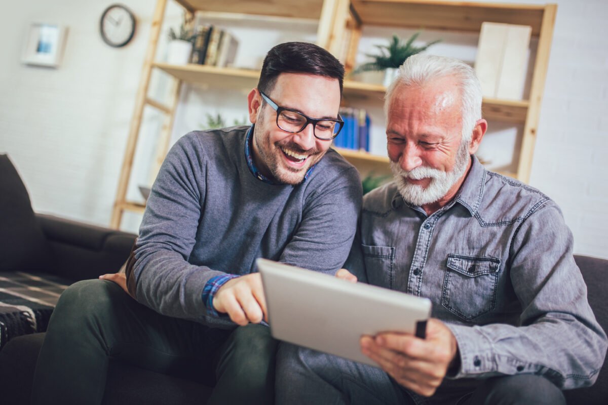 Life Settlement: senior man with adult son using digital tablet at home