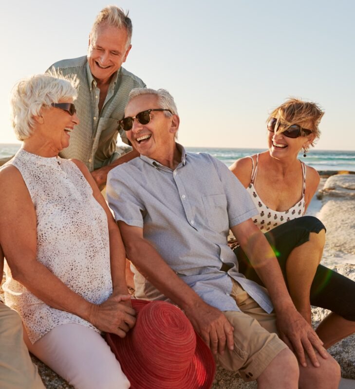Life Settlements: Group Of Senior Friends Sitting On Rocks By Sea On Summer Group Vacation