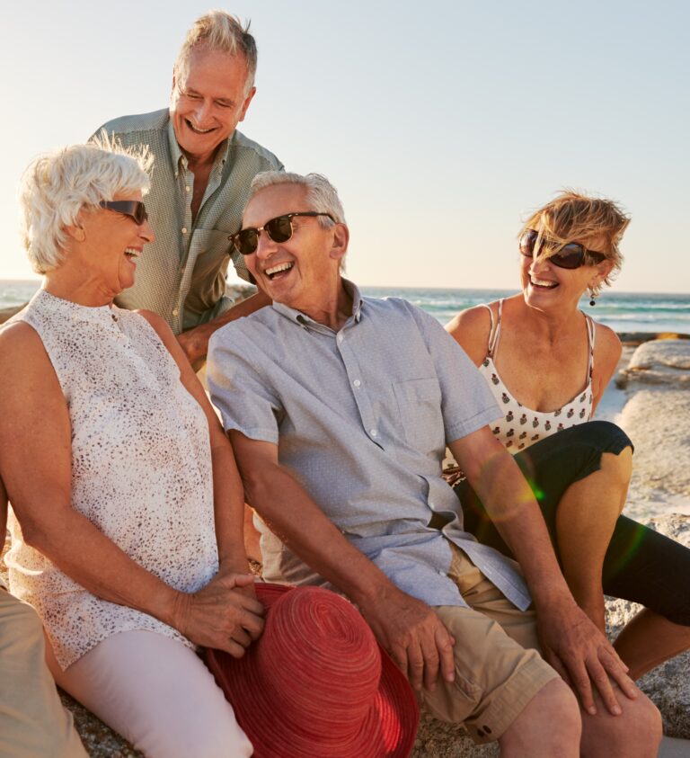Life Settlements: Group Of Senior Friends Sitting On Rocks By Sea On Summer Group Vacation