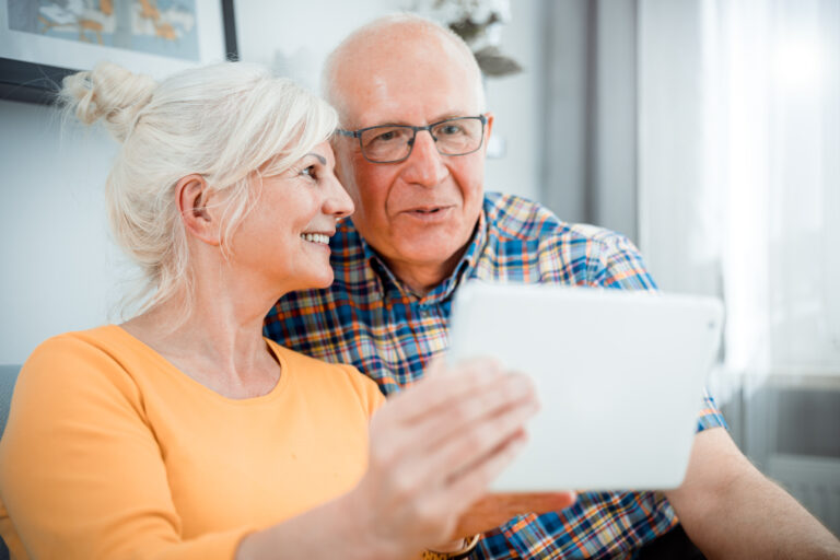 Life Settlement Calculator: Happy senior couple looking at tablet sitting on sofa at home