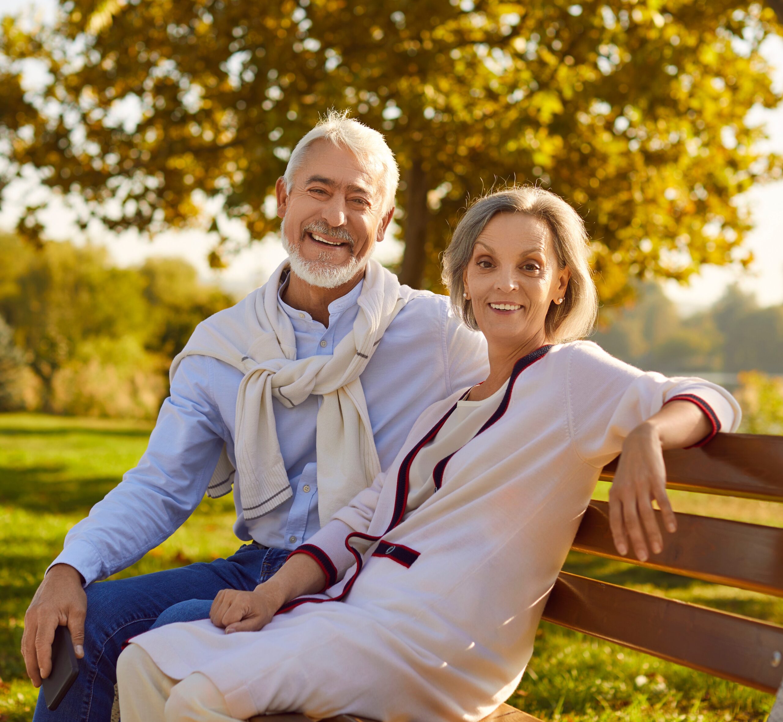 Selling a life insurance policy: Portrait of happy married senior couple sitting on bench in beautiful green summer park
