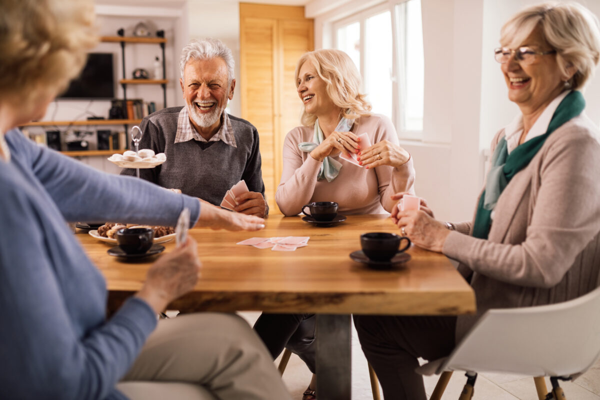 Life Settlement Providers: Cheerful senior friends playing cards while gathering at home.